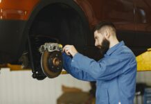 Mechanik w niebieskim kombinezonie naprawia hamulce w warsztacie