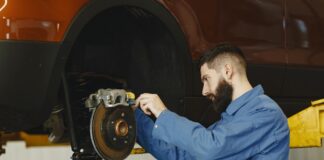Mechanik w niebieskim kombinezonie naprawia hamulce w warsztacie