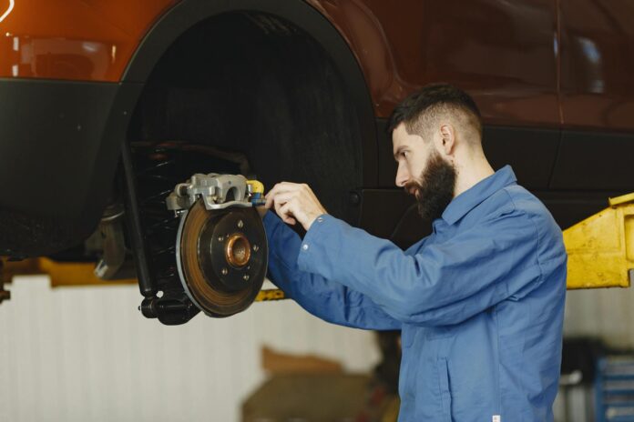 Mechanik w niebieskim kombinezonie naprawia hamulce w warsztacie Mechanik w niebieskim kombinezonie naprawia hamulce w warsztacie